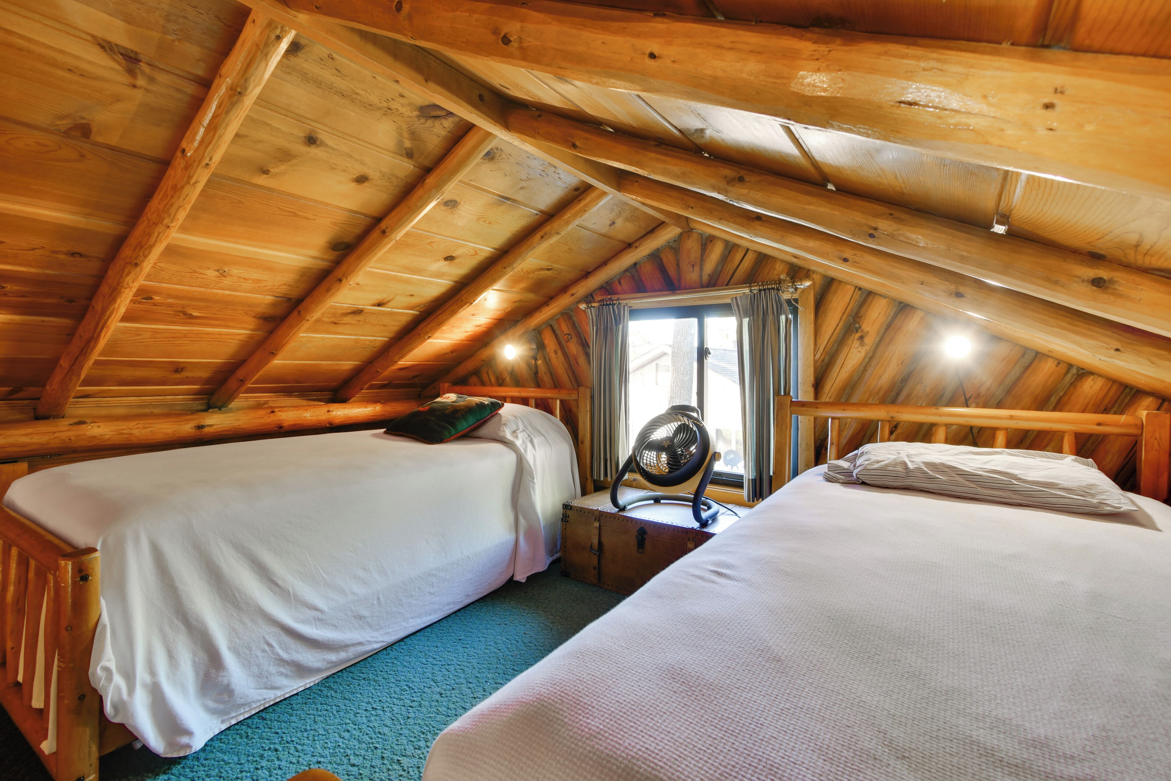 A room with two beds, a window with curtains, and a ceiling fan.