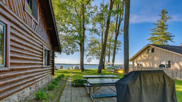 Una cabaña de troncos con un patio, mobiliario exterior y vistas al lago.