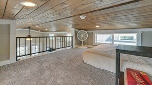 Ein Zimmer mit schrägem Dach, einem Standventilator, einem Bett und einem Fenster.