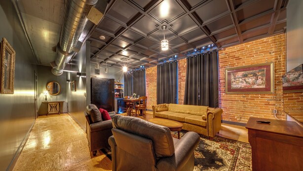 Una habitación con pared de ladrillo, un sofá, un sillón de cuero, una mesa de centro y una alfombra.