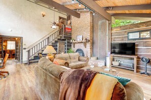 A cozy living room with a fireplace, a television, and a staircase leading to another level. - Walk to Dtwn Sonora! Rustic Creekfront Cabin (Sonora)