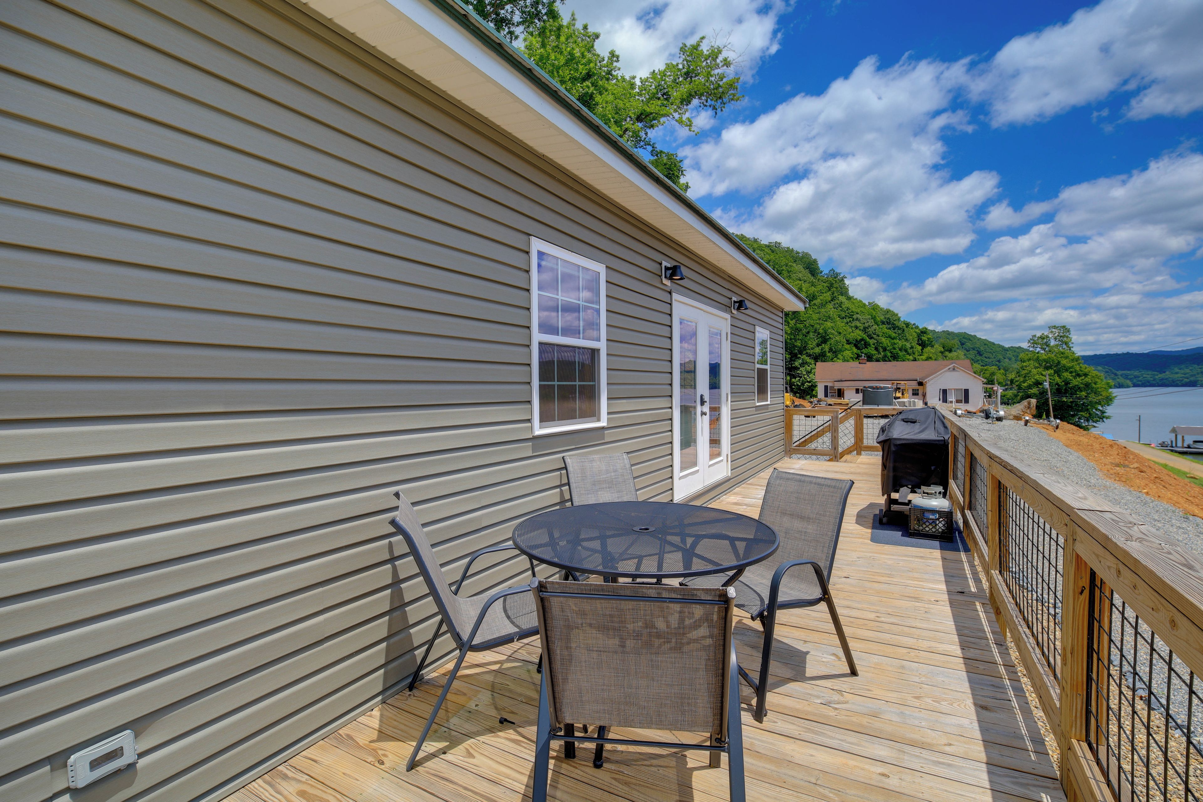 A deck with a table and chairs, a covered grill, and a view of a lake.