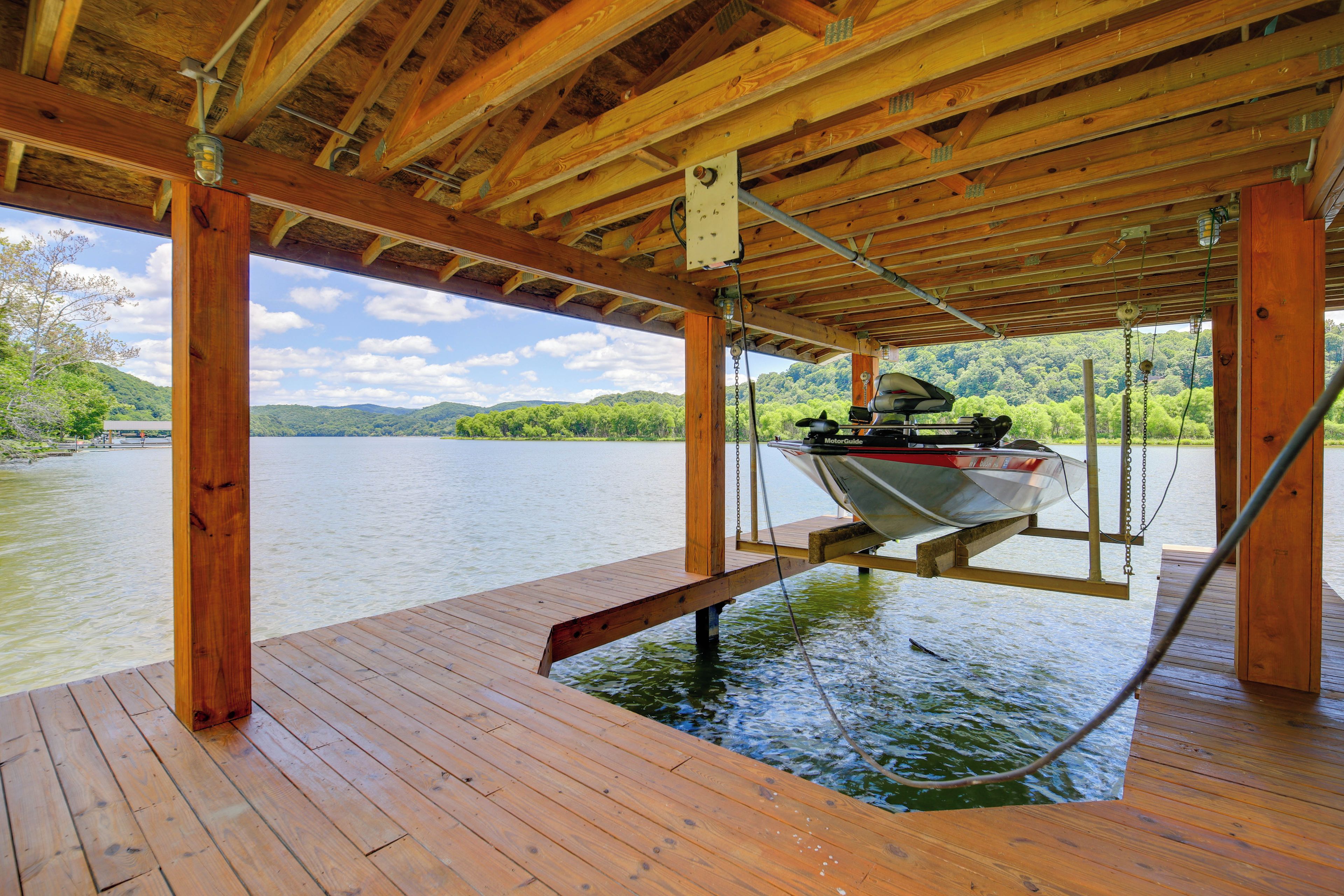 A wooden deck with a boat suspended by chains, a metal railing, and a view of a lake with hills in the background.