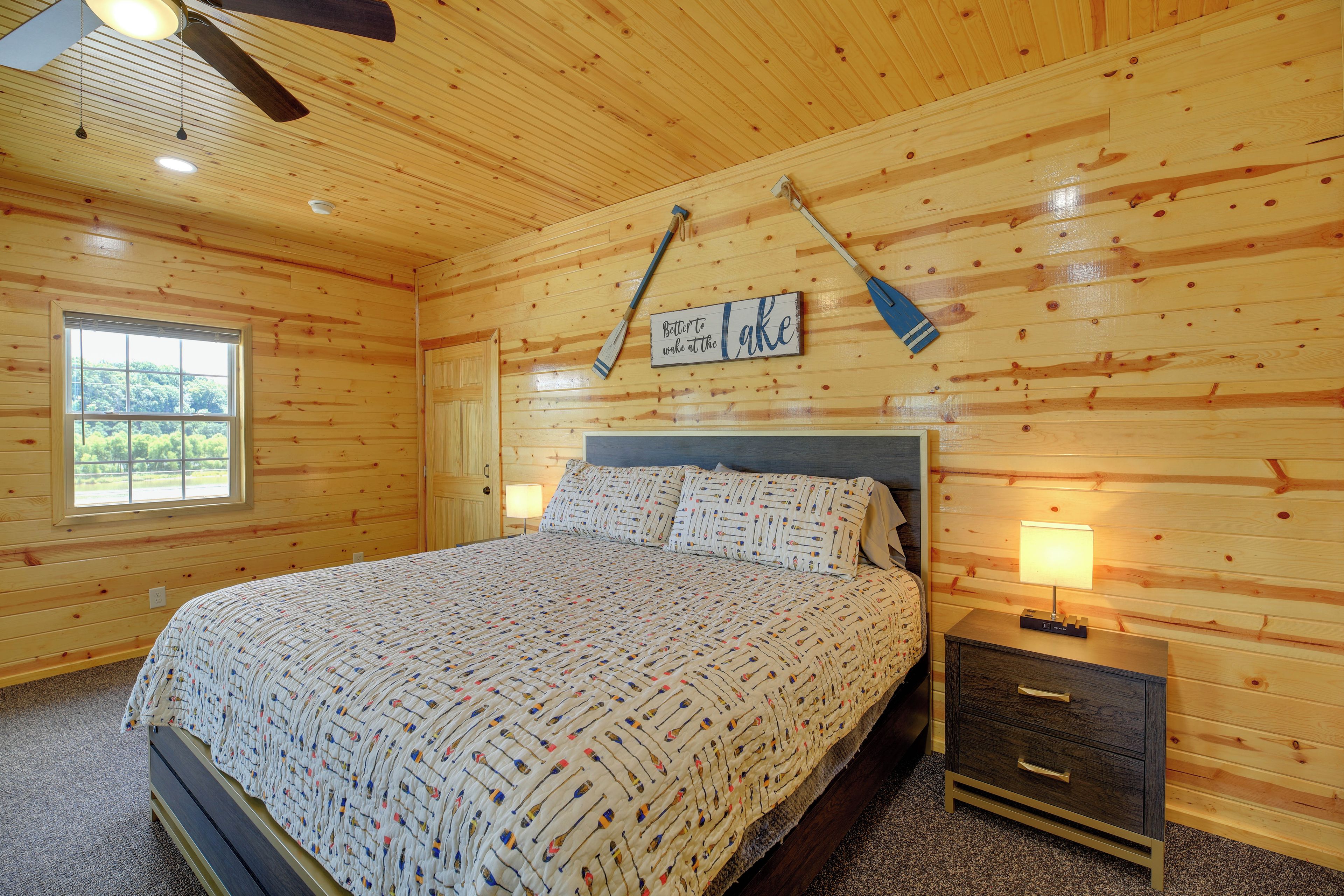 Quarto de cabana de madeira com uma cama, duas luminárias de cabeceira, uma mesinha de cabeceira e uma janela.