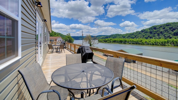Una terraza con mobiliario exterior, una parrilla y vista a un río y bosque.