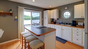 A kitchen with a bar area, white cabinets, a window, and a view of greenery. - Fire Pit & Floating Dock! Claytor Lake Hideout (Draper)