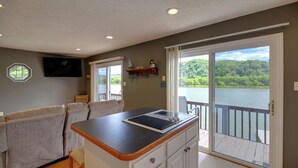A kitchen with a large island, a dining area with a sofa, and a view of a lake through a sliding door. - Fire Pit & Floating Dock! Claytor Lake Hideout (Draper)