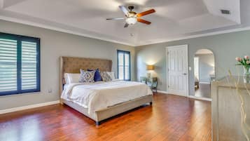 Un dormitorio con cama, ventilador de techo, piso de madera y una puerta.