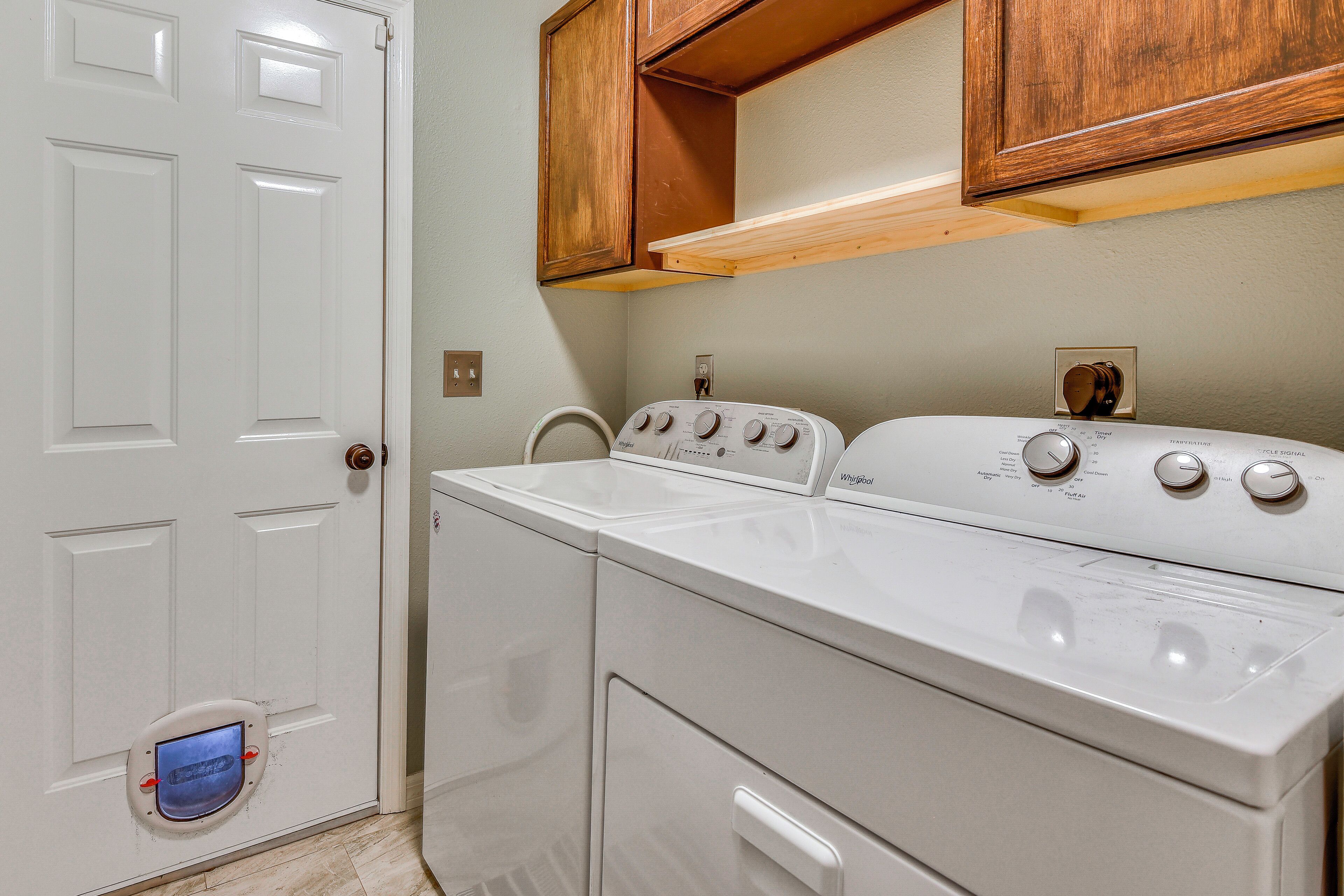 A laundry area with a front-loading washer and dryer, wooden cabinets above, and a white door.