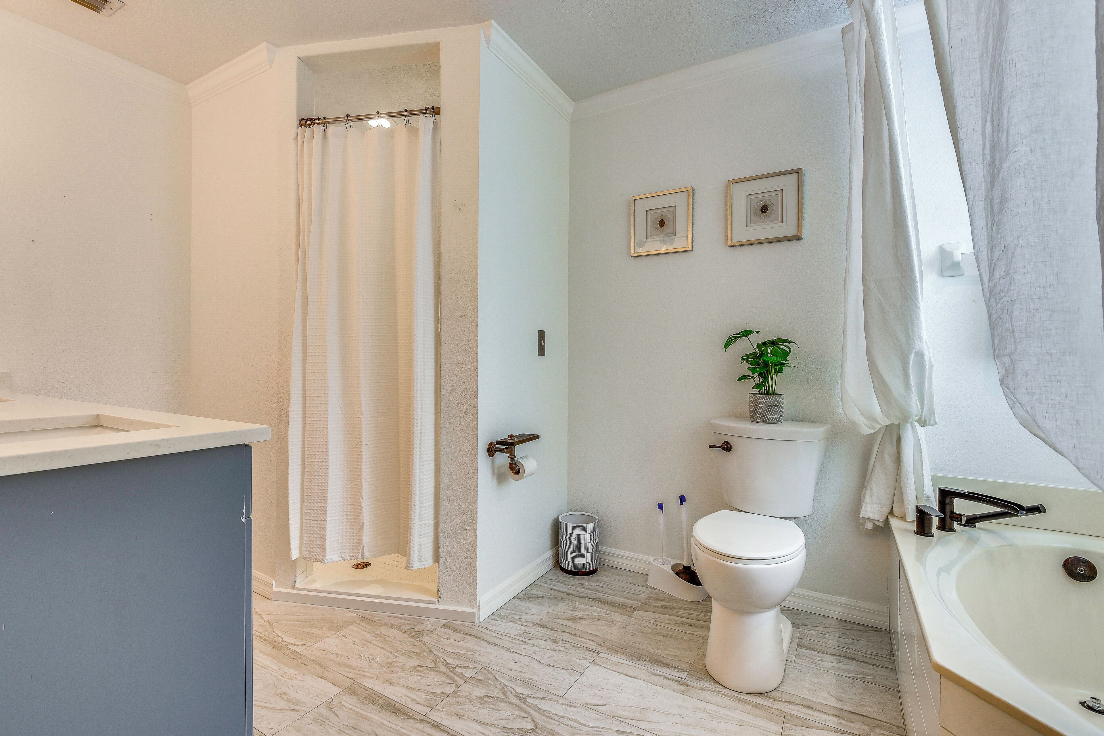 A bathroom with a shower, toilet, sink, and two framed pictures on the wall.