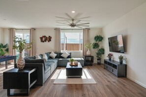 A living room with a sectional sofa, a coffee table, a TV, and potted plants. - Modesto Area Family Getaway w/ Patio & Backyard! (Modesto)