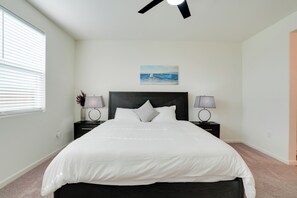 A bedroom with a bed, two bedside tables, a ceiling fan, a painting, and a window with blinds.