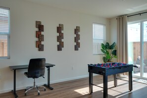 Een kamer met een tafelvoetbaltafel, twee bureaus, een stoel en decoratieve muurdecoratie.