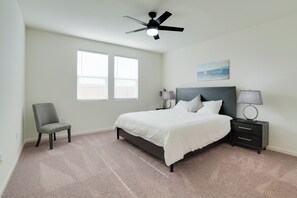 Ein Schlafzimmer mit einem Bett, Nachttischen, einem Sessel, einem Deckenventilator und einem Fenster.