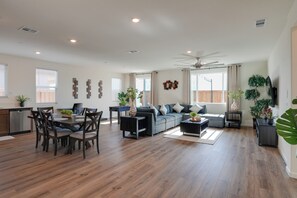 Ein geräumiger Wohnbereich mit Esstisch, Sofa, Sesseln, Deckenventilator und Küchenzeile mit Geschirrspüler.