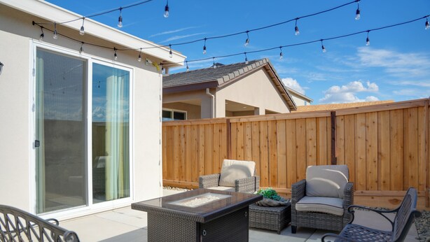 An outdoor patio with wicker furniture, a glass-top table, and string lights. - Modesto Area Family Getaway w/ Patio & Backyard! (Modesto)