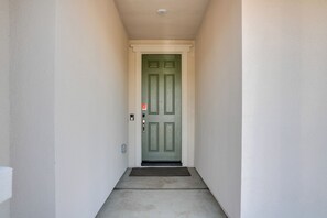 A narrow hallway with a green door, a doormat, and a light switch on the wall. - Modesto Area Family Getaway w/ Patio & Backyard! (Modesto)