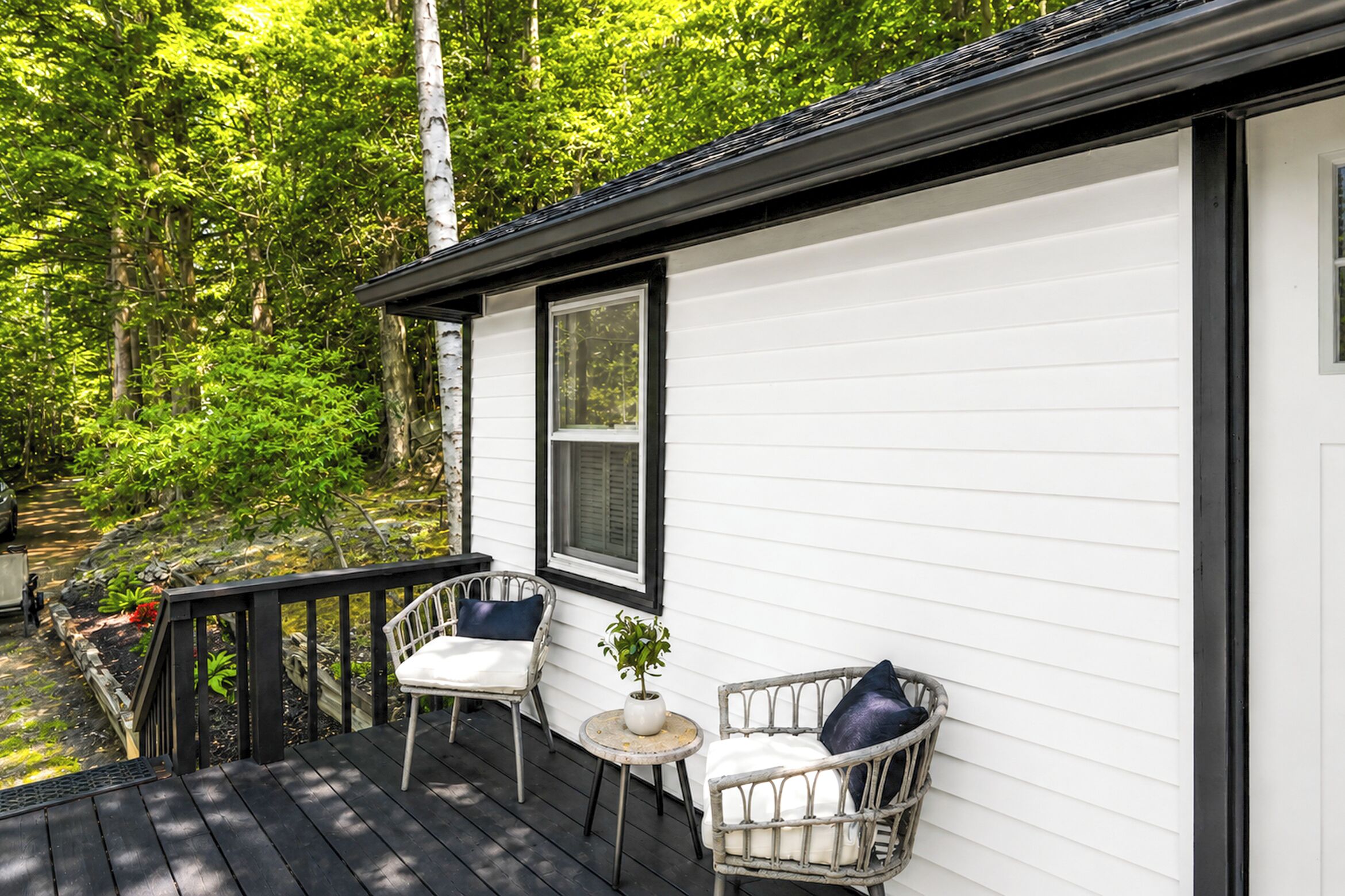 Eine Holzterrasse mit zwei Korbstühlen und einem kleinen Tisch mit einer Pflanze.