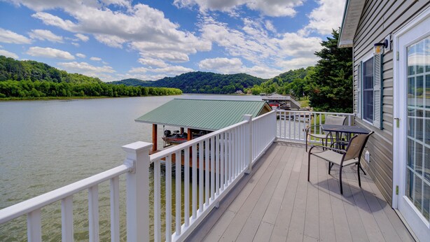 A deck with a view of a lake and mountains, a table and chairs, and a building with a green roof. - Waterfront Deck w/ Mtn View! Claytor Lake Retreat (Draper)