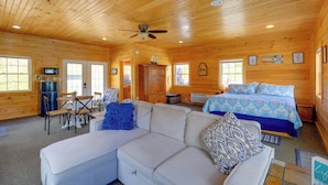 A log cabin interior with a sofa, a bed, a dining table, and a ceiling fan. - Waterfront Deck w/ Mtn View! Claytor Lake Retreat (Draper)