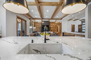 A modern kitchen with marble countertops, a central island, and pendant lighting. - NC420 | 56399 Elk Run Drive (Sunriver)