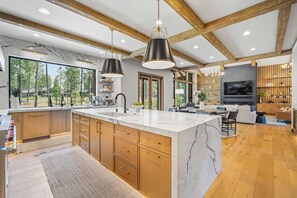 A modern kitchen with a large island, wooden cabinets, and a view of the outdoors. - NC420 | 56399 Elk Run Drive (Sunriver)
