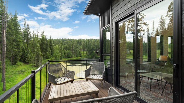 Un balcon doté de meubles en osier, d’une table en bois et d’une porte vitrée donnant sur un espace intérieur avec des sièges supplémentaires.