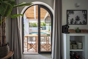 A room with a large arched doorway leading to an outdoor pool area, a wooden table and chairs, and a shelf with plates and wine bottles. - Authentic hacienda near the Mediterranean Sea (VC)