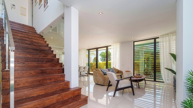A modern interior with a wooden staircase, a living area with a sofa and coffee table, and large glass doors leading to an outdoor area. - Bright Artistic 4-Bedroom Home in Faro | Newly Refurbished | 3 Bathrooms (Faro)