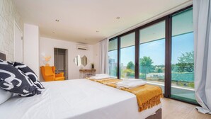 A modern bedroom with a large bed, a chair, and a view of the outdoors. - Bright Artistic 4-Bedroom Home in Faro | Newly Refurbished | 3 Bathrooms (Faro)