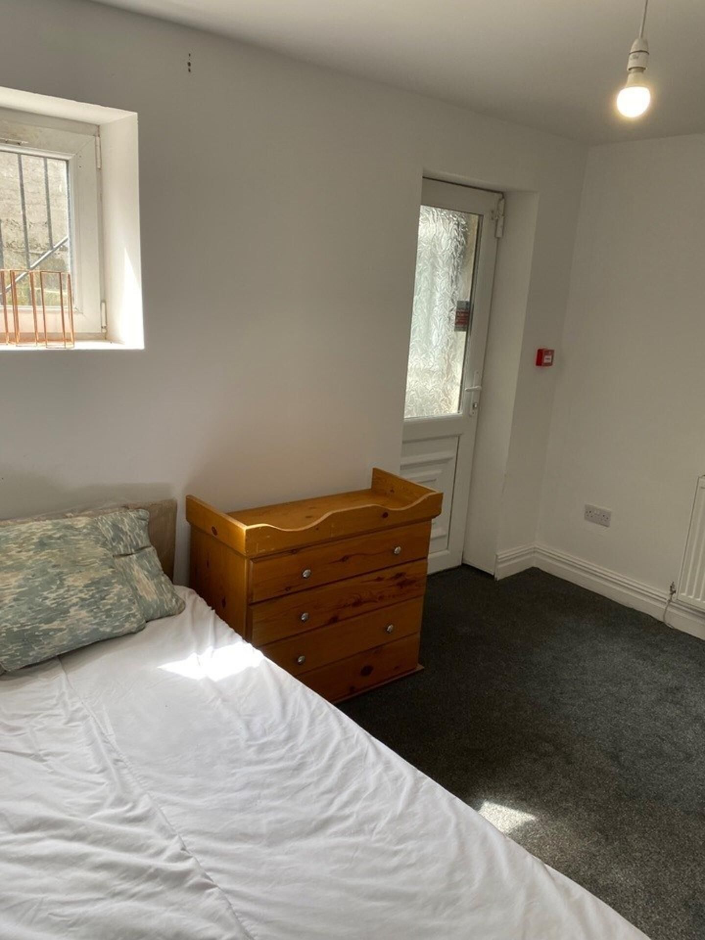 A bedroom with a bed, a wooden dresser, a window with blinds, and a door.