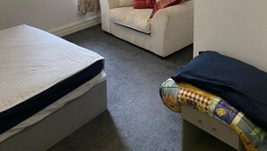 A small, sparsely furnished room with a single bed, a sofa, and a window with curtains. - House 2 Bedrooms Sleeps 4 With Parking (Bolton)