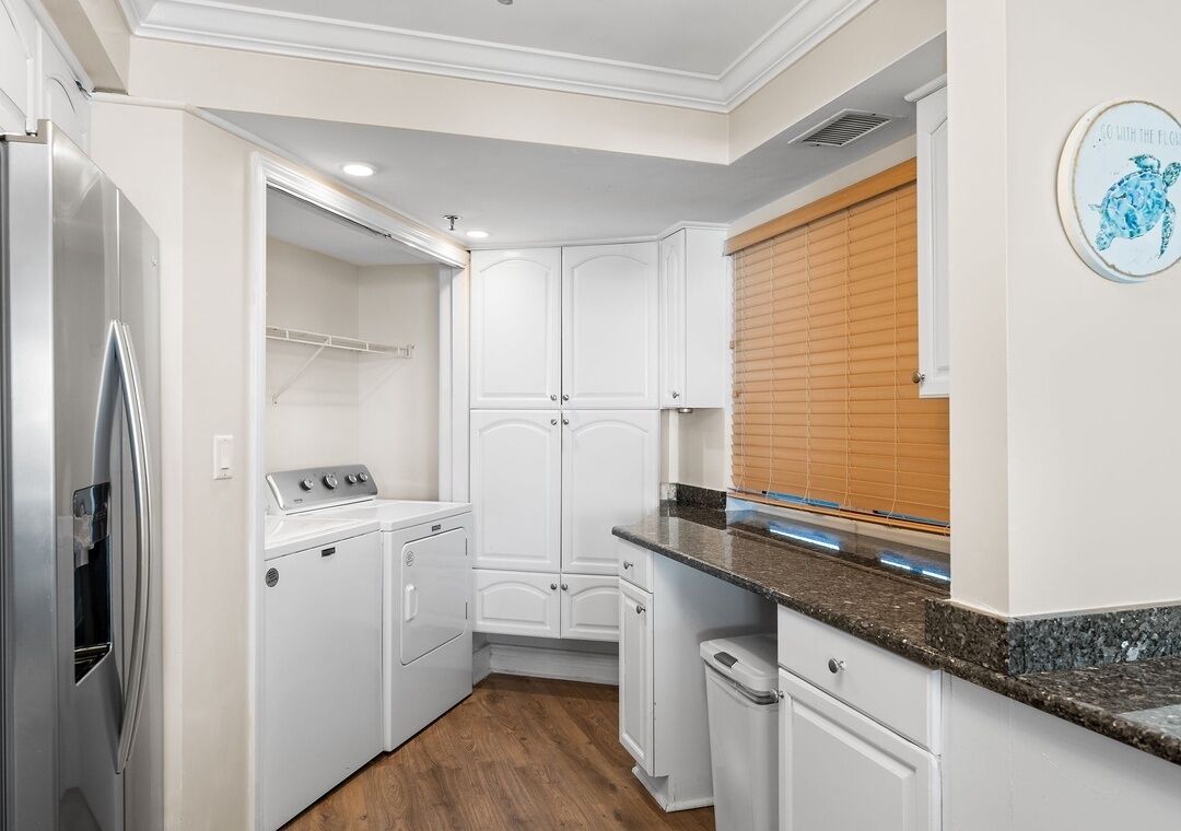 A compact kitchen with white cabinetry, a stainless steel refrigerator, a built-in washer and dryer, and a granite countertop.