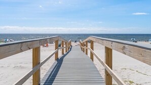 Una passerella di legno conduce a una spiaggia sotto un cielo sereno.