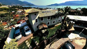 Ein Haus mit geneigtem Dach, ein geparktes Auto davor und im Hintergrund Meer und Berge.
