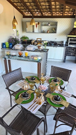A dining area with a glass-top table set for six, surrounded by wicker chairs. - A Casa Bella Guest House - Ilhabela (Ilhabela)
