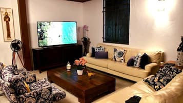 A living room with a television, sofa, coffee table, and patterned chairs.
