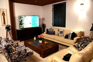 A living room with a television, sofa, coffee table, and patterned chairs. - A Casa Bella Guest House - Ilhabela (Ilhabela)