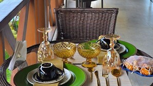 A dining table set with green plates, gold cutlery, and glassware on a wicker chair. - A Casa Bella Guest House - Ilhabela (Ilhabela)