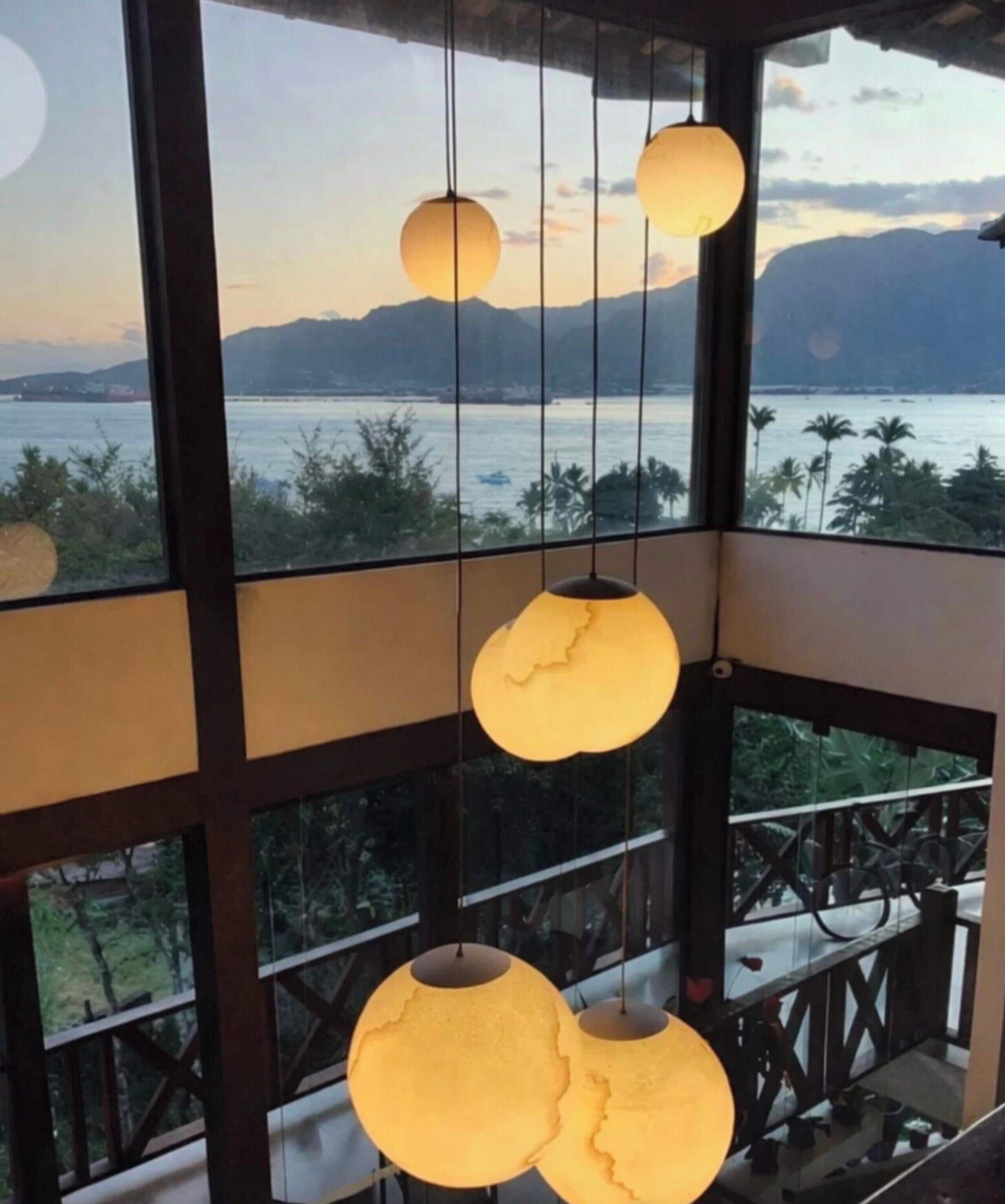 A room with large windows overlooking a body of water and mountains. There are hanging spherical light fixtures.