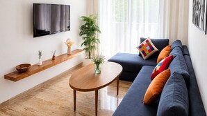 Una sala moderna con un televisor de pantalla plana, un sofá azul oscuro, una mesa de centro de madera y una planta en maceta.