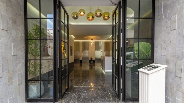 Entrada de hotel con puerta de cristal, suelo de mármol y mostrador de recepción con teclado.