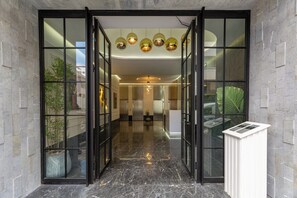 Entrada de hotel con puerta de cristal, suelo de mármol y mostrador de recepción con teclado.