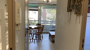 Ein Flur, der in einen Essbereich mit Tisch und Stühlen führt, mit einer Deckenleuchte und einem Fenster mit Jalousien.