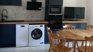 Eine kleine Küche mit Waschmaschine, Mikrowelle, Backofen und einem Essbereich mit Stühlen.