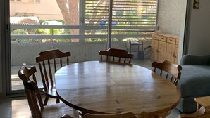Ein Zimmer mit einem runden Holztisch, vier Stühlen, einem Sofa, einer Kommode und einem großen Fenster mit Jalousien.
