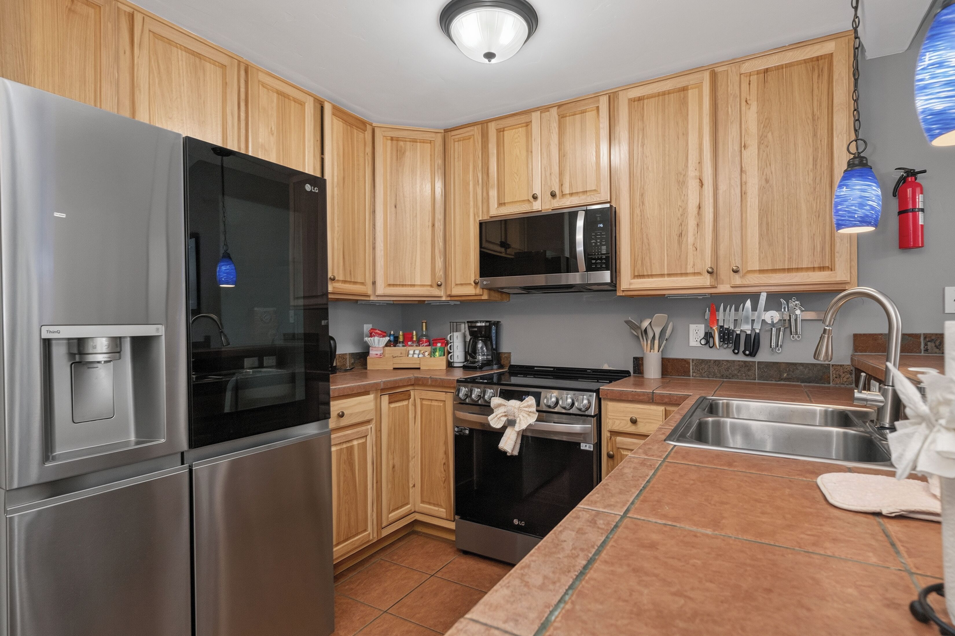 A kitchen with stainless steel appliances, wooden cabinets, a tiled backsplash, and a hanging light fixture.