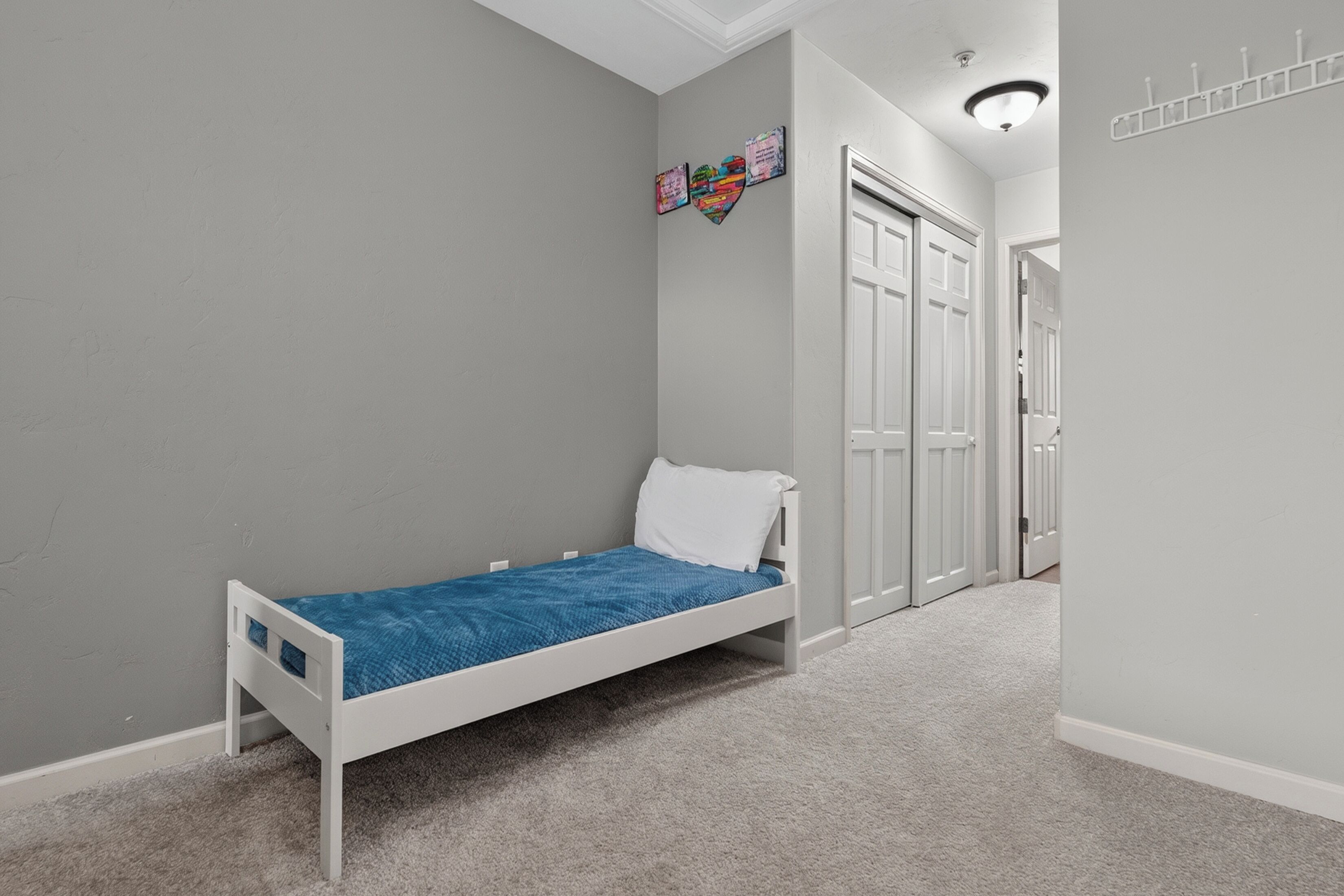 A room with a single white bed, grey walls, and a door leading to another room.