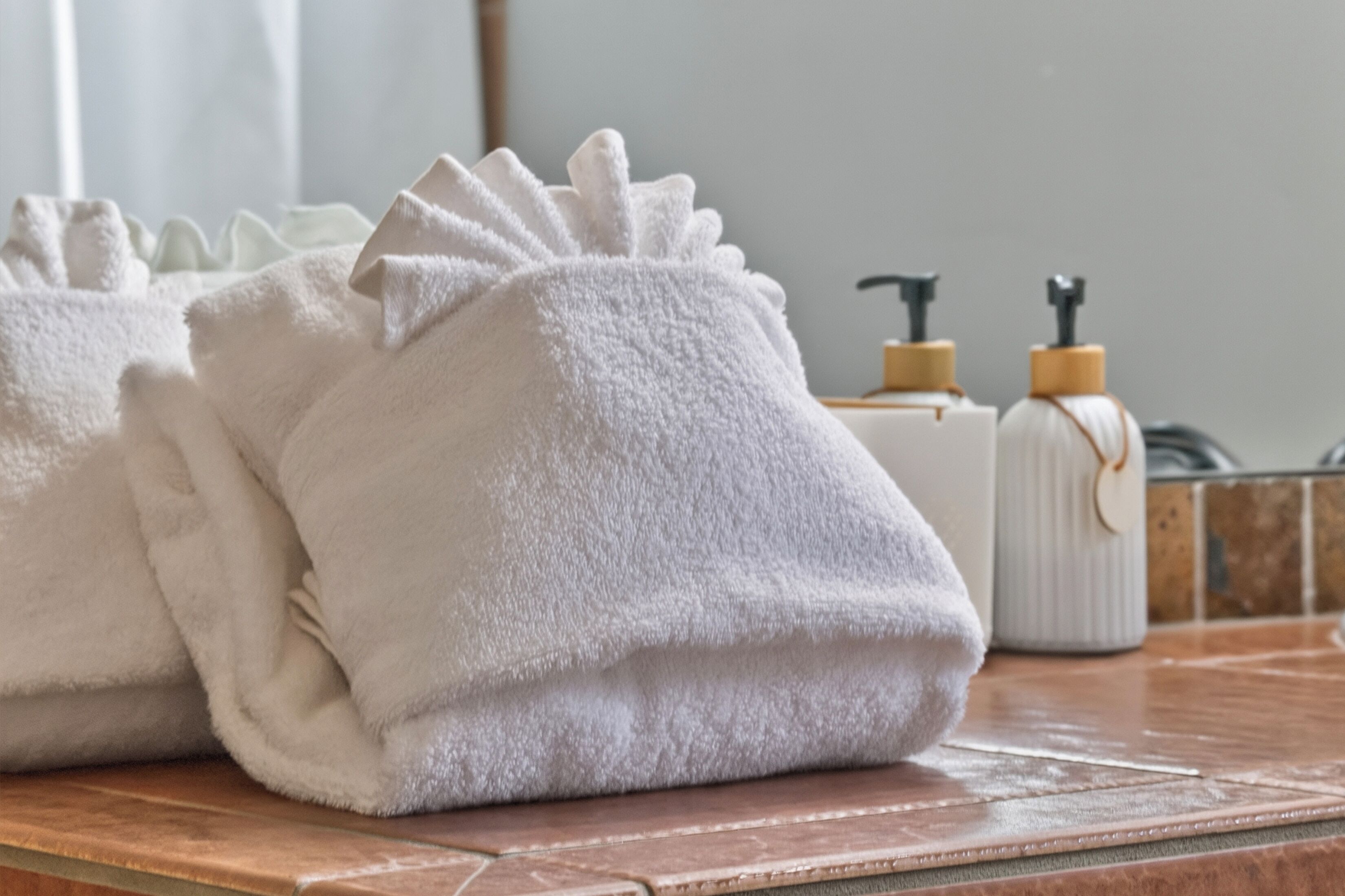 Neatly folded towels on a bathroom counter, a soap dispenser, and a white bottle with a pump.