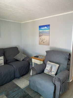 Un salón con dos sofás grises, una mesita de madera y un cuadro colgado en la pared de una playa.